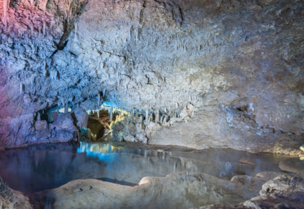 Harrison's Cave interior in Barbados with stalactites, crystal-clear subterranean pool, and illuminated limestone formations on a shore excursion from Bridgetown cruise port.
